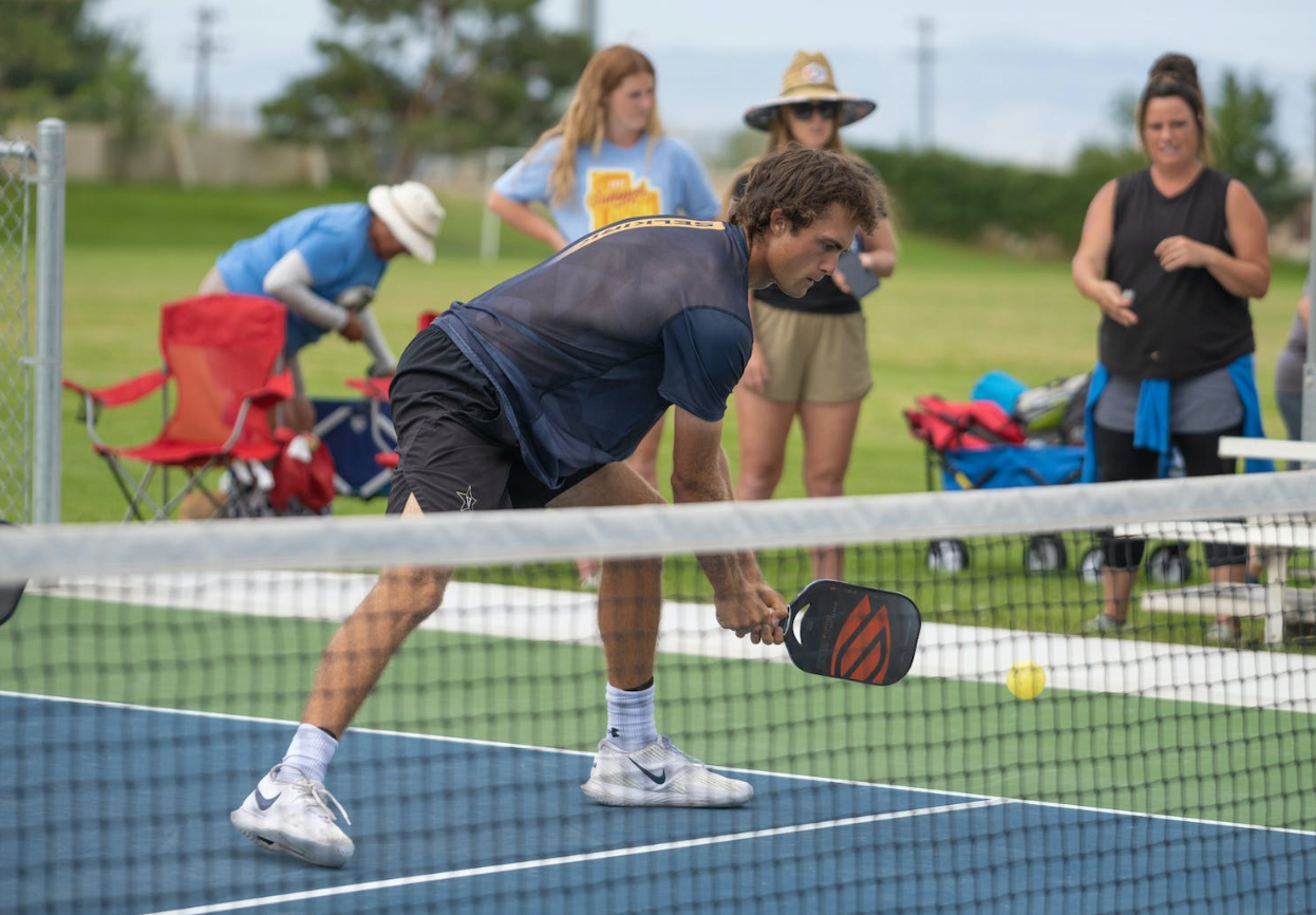 A player practicing pickleball, preparing to hit a ball with a paddle, surrounded by spectators.