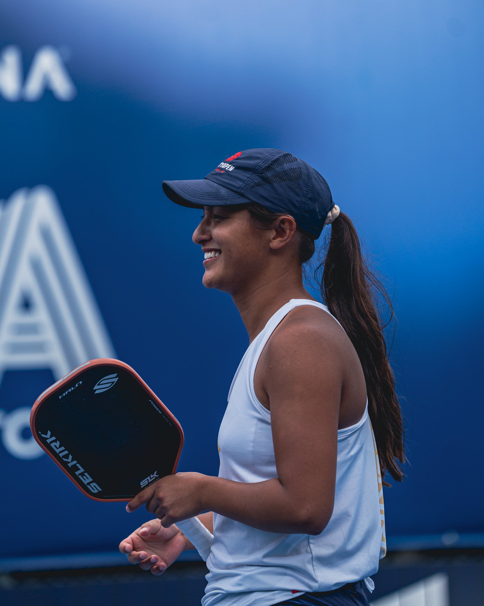 Professional pickleball player Jackie Kawamoto smiles as she holds her SLK Halo paddle on an outdoor court.