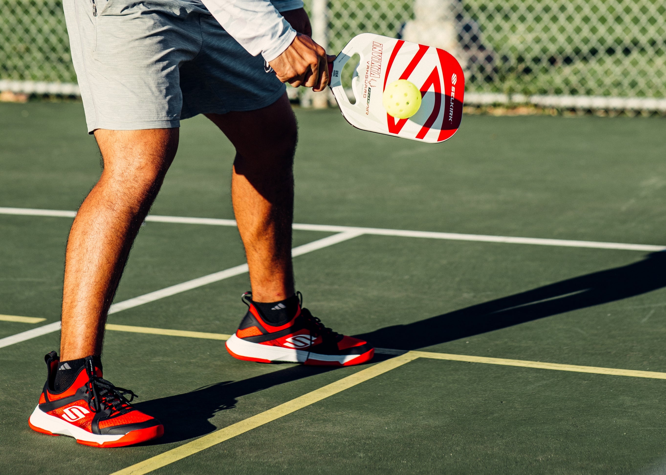 Red and black Selkirk pickleball shoes with Selkirk pickleball paddle.