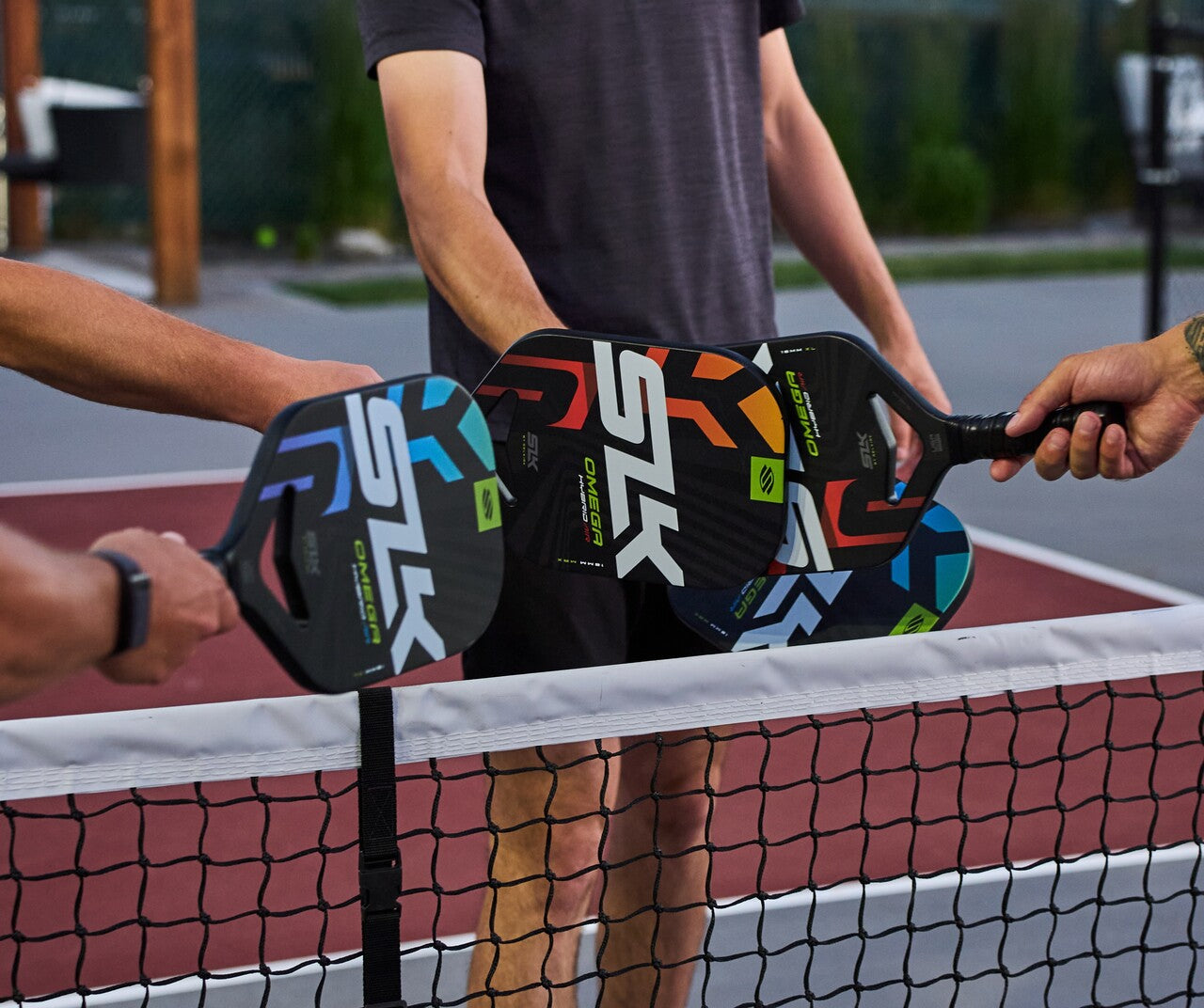 Four players tap their different paddles over the pickleball net on an outdoor court.