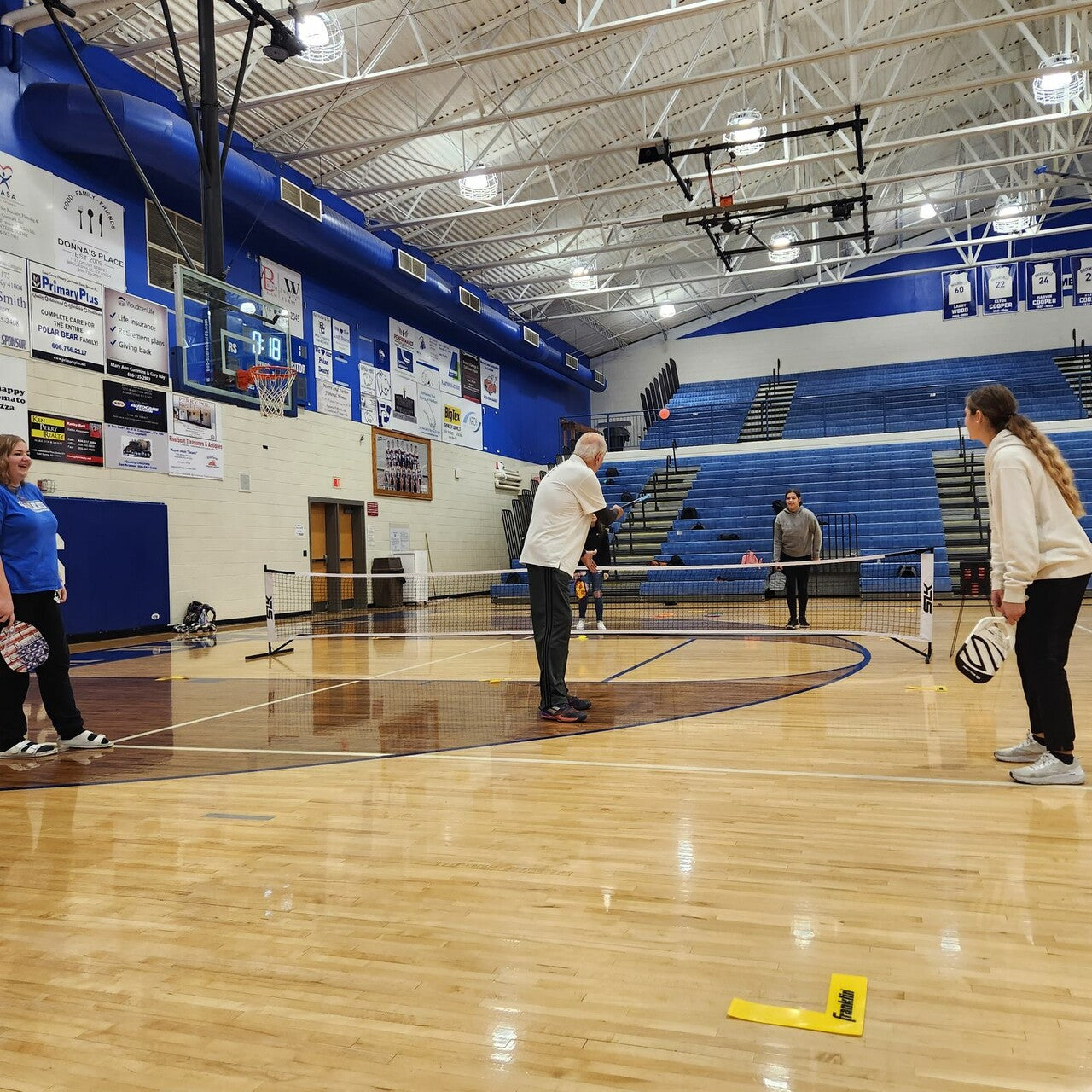 Pickleball players use Selkirk paddles and nets to play pickleball on an indoor basketball court.