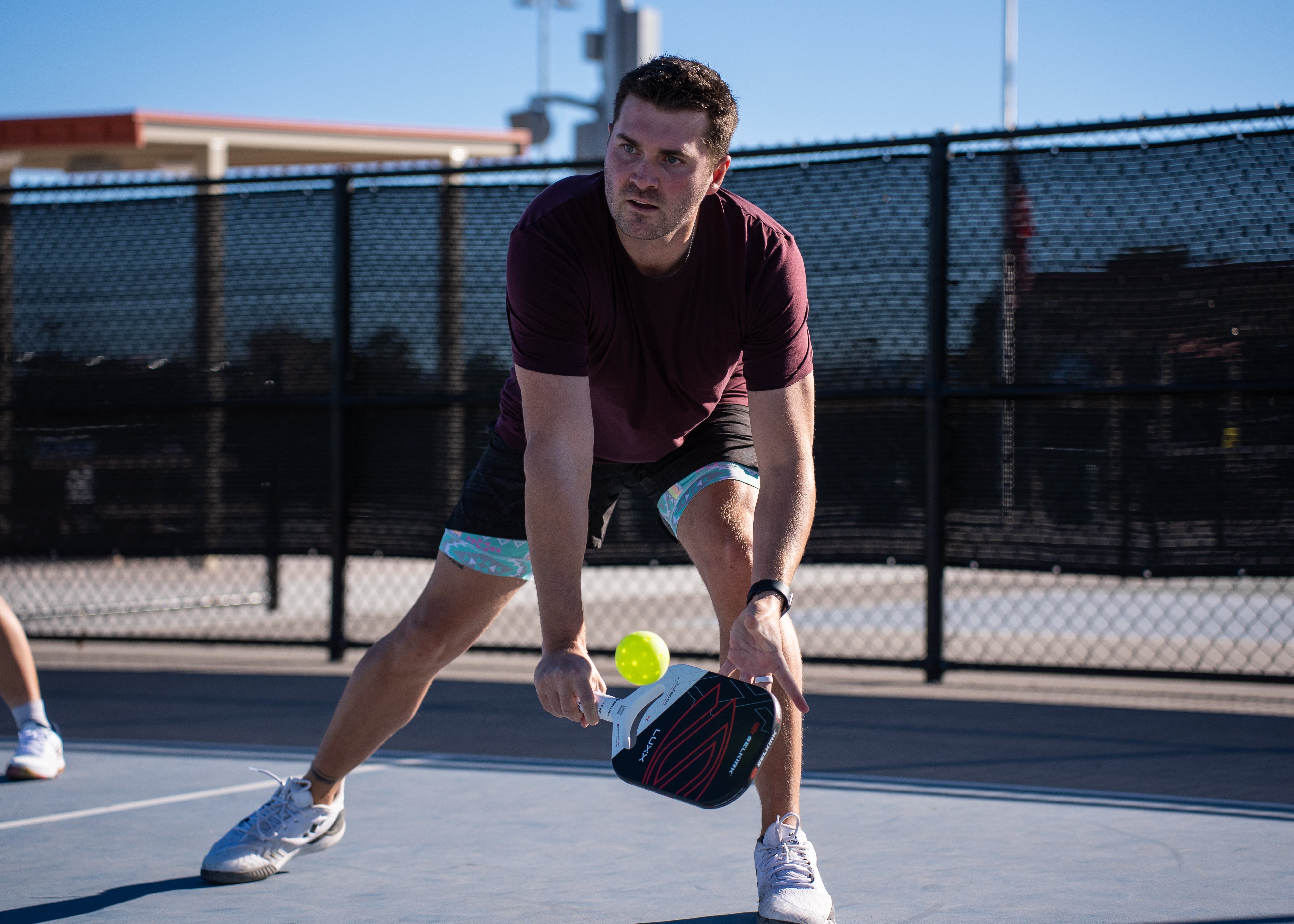 A man lunges for a wide pickleball dink on an outdoor pickleball court. 