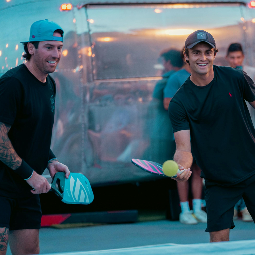 James Neal and James Ignatowich track a pickleball on an outdoor pickleball court. 