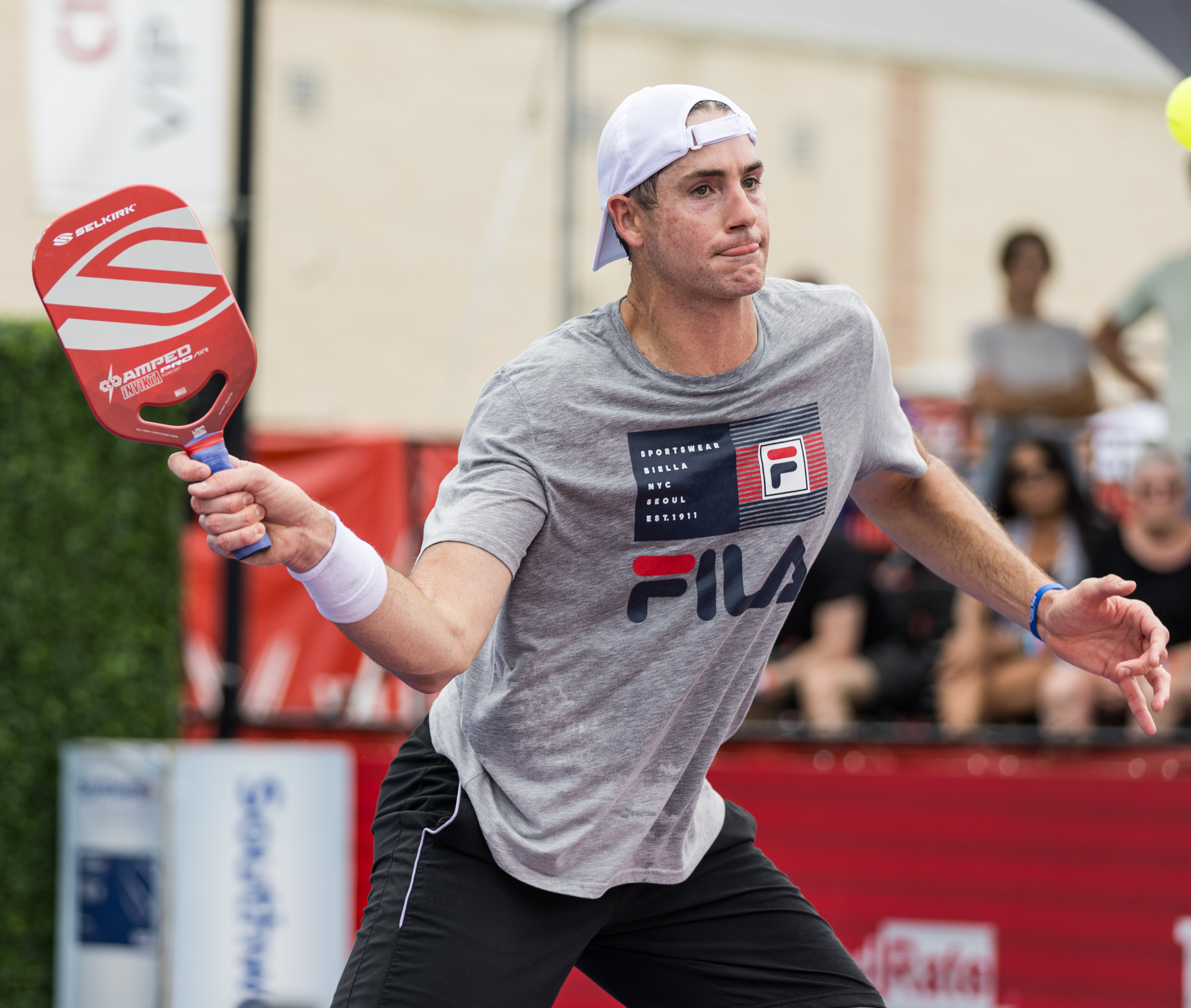 Action shot of John Isner with clickable dots to shop the products they are using and wearing.