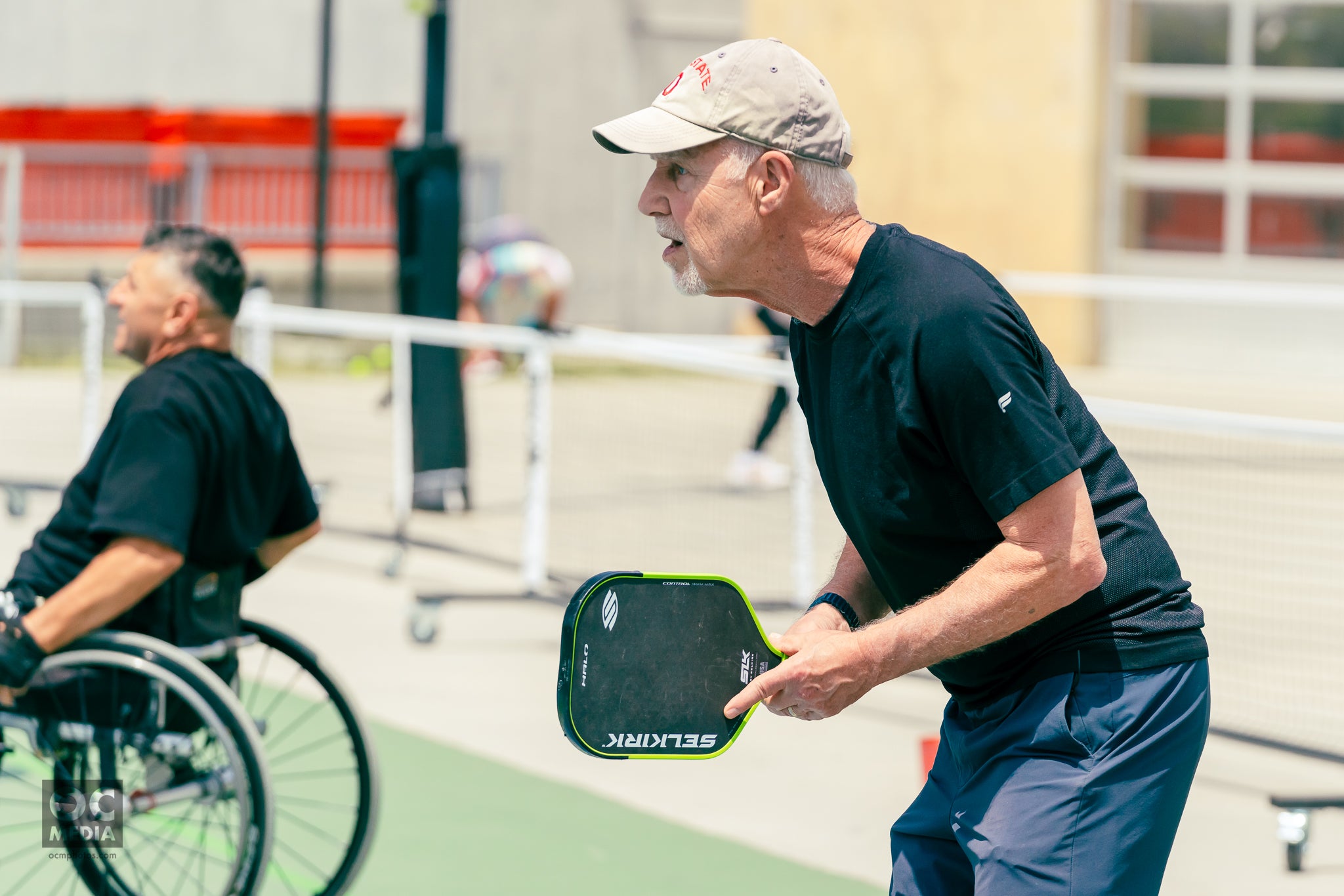 A profile shot shows a man prepared to receive a pickleball shot. He is holding a SLK Halo paddle. 