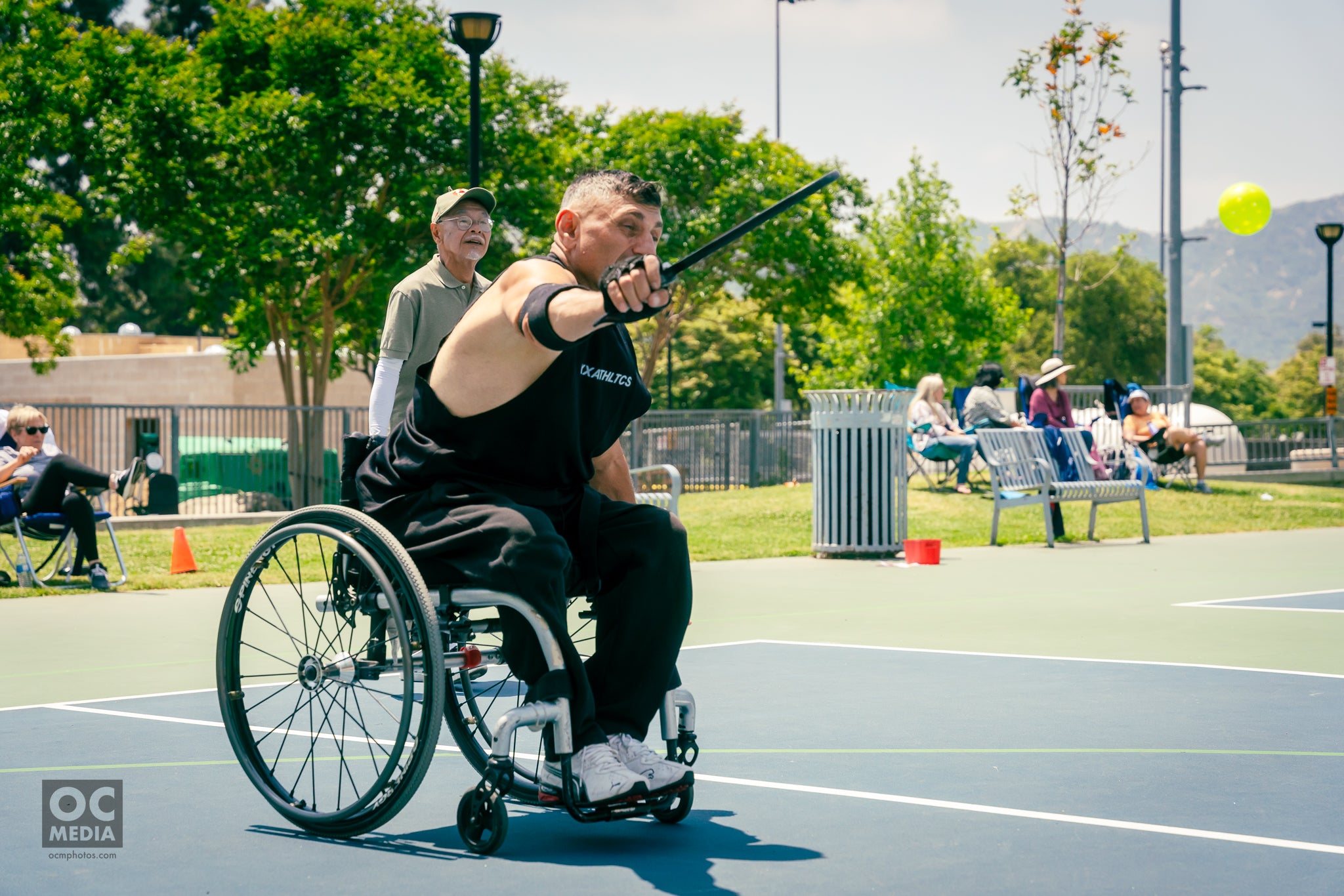 A pickleball player uses a wheelchair while hitting a pickleball over a net. 