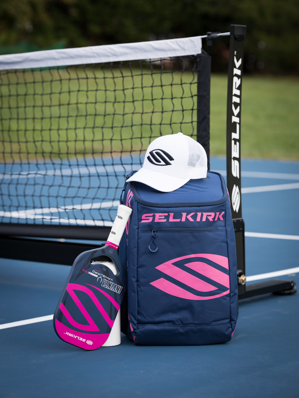 Selkirk Sport Prestige pickleball bags in navy blue and pink, with a Selkirk pickleball paddle, hat, and pickleball net.